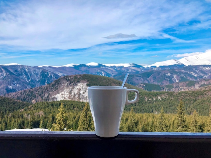 Photo white cup placed on wooden railing on the balcony with view of snowcapped mountains
