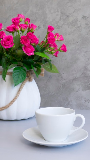 White cup and saucer on the table against the background of a bouquet of flowers