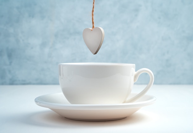 A white Cup and saucer with a wooden white heart hanging on top