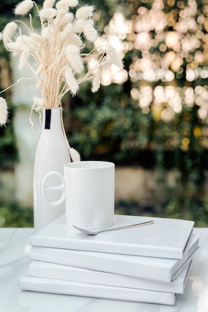 White cup and spoon on white books with bokeh of sunlight