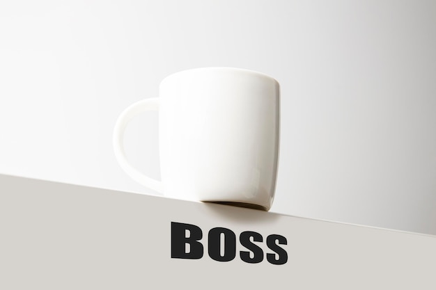 White cup stands on the edge of the table with the inscription boss on a white background