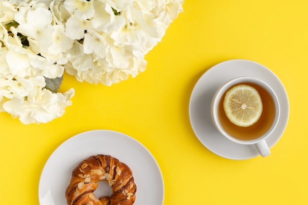 White cup of tea and flowers on yellow background. Flat lay top view breakfast concept