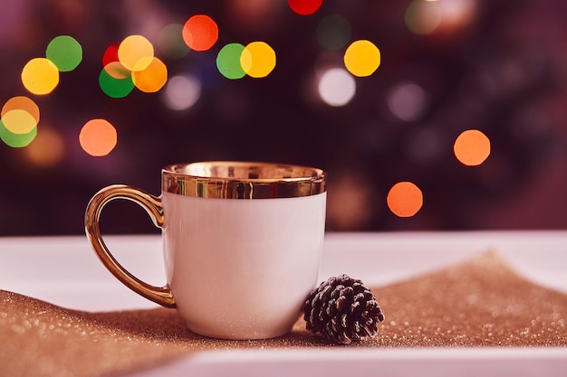 White cup of tea in front of Christmas tree Cup mock up with cone Traditional holidays coziness