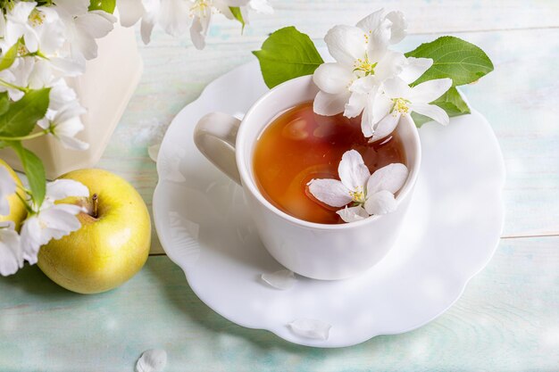 アップルツリーの花と木製のテーブルの黄色いリンゴで形状の皿に白いカップの茶