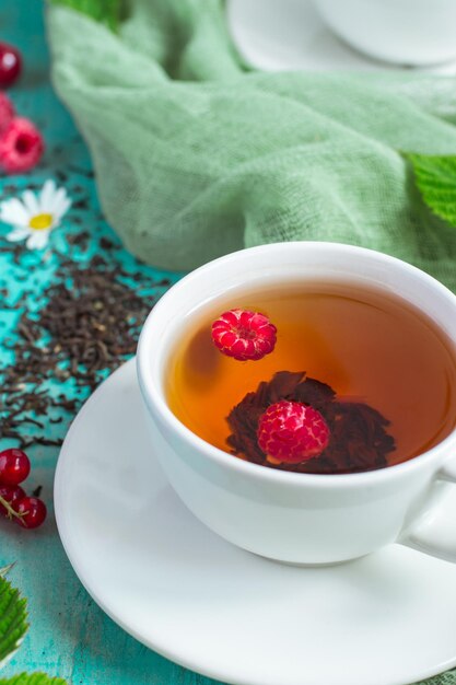 White cup of tea with raspberries closeup  on a turquoise background