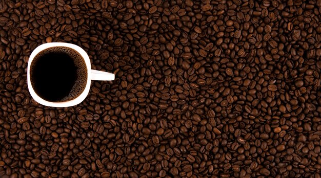 A white cup with Americano on roasted coffee beans View from above Coffee background