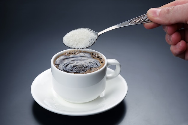 White cup with black coffee and spoon with sugar