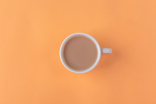 White cup with black coffee with milk on orange background. Minimalism, Copy space for text. Autumn flat lay composition.