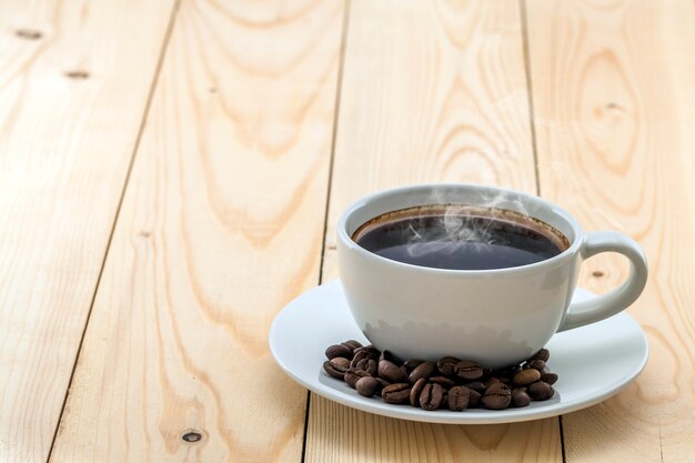 White cup with black steaming coffee on plate with coffee beans on yellow