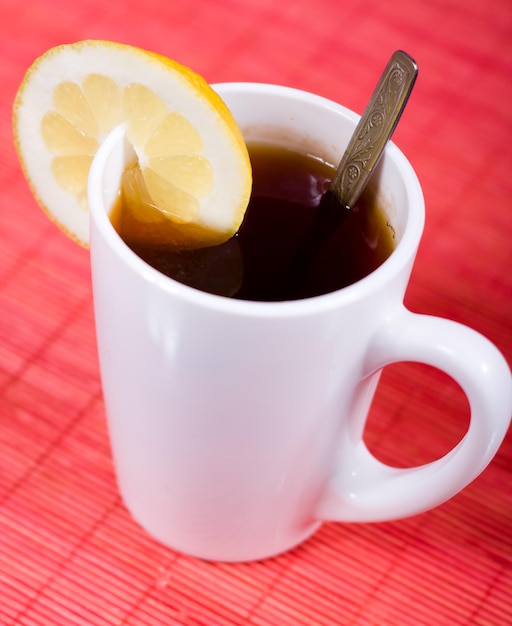 White cup with black tea and piece of lemon