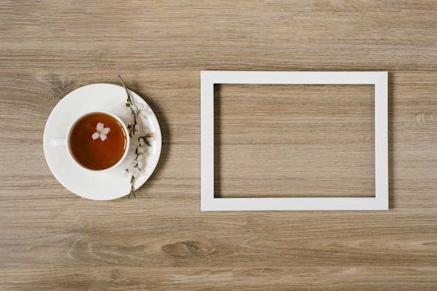 A white cup with black tea and a sprig of apple blossom and a white frame on a wooden background. Mocap and up prostranstva