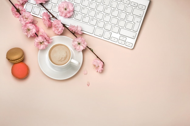 Tazza bianca con cappuccino, fiori di sakura, tastiera su uno sfondo rosa pastello