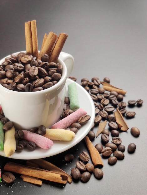 Белая чашка с кофе в зернах и цветной мармелад на черном фоне