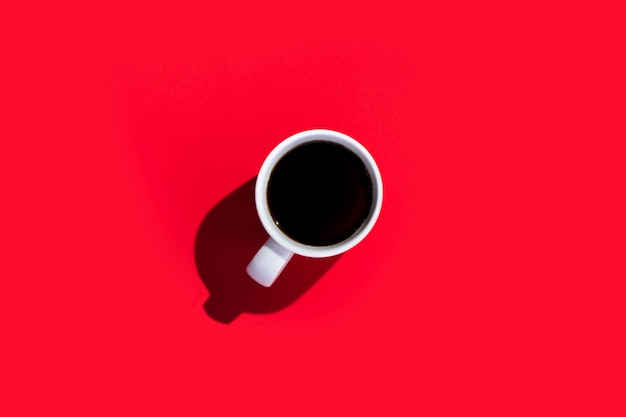 White cup with a coffee on a isolated red space. Top view, flat lay