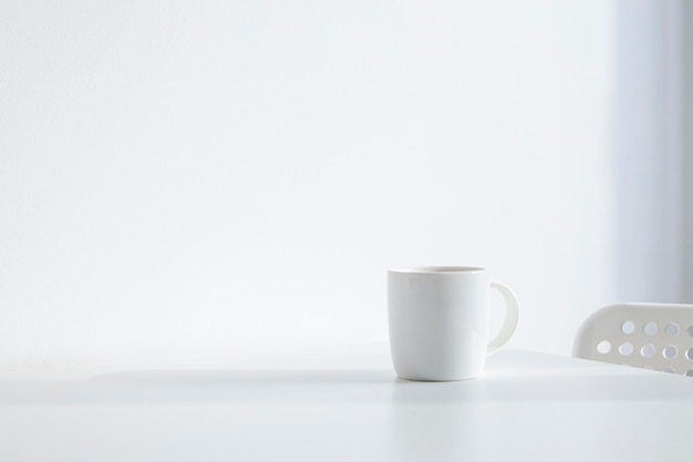 White cup with coffee on a white table under natural light