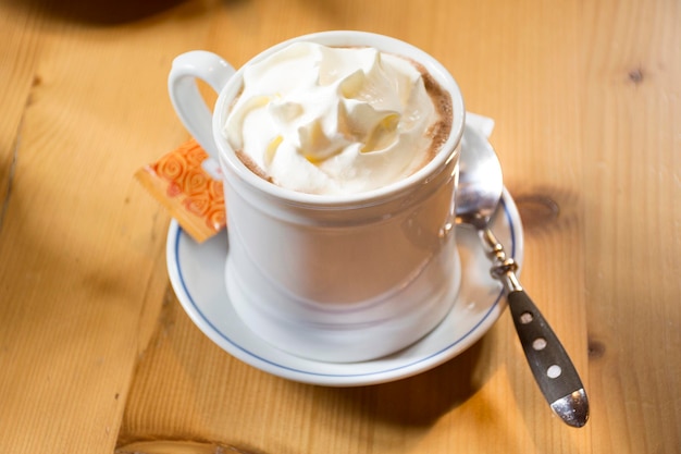 White cup with hot chocolate topping whipped cream serve with sugar bag for Swiss and travelers people eat and drink in restaurant at Samnaun village in Graubunden Switzerland