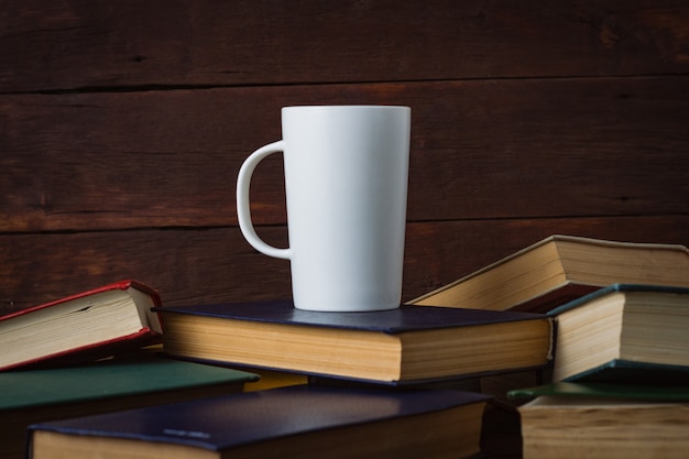 Tazza bianca con caffè caldo su libri distribuiti su una parete di legno scuro