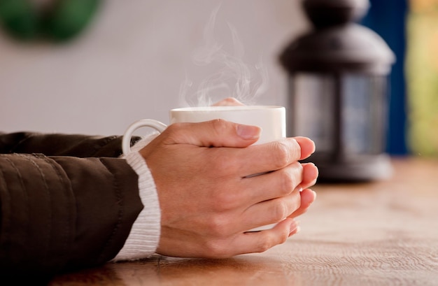 Tazza bianca con bevanda calda e mani fumanti che si scaldano dal caldo di casa concentrati sulla tazza