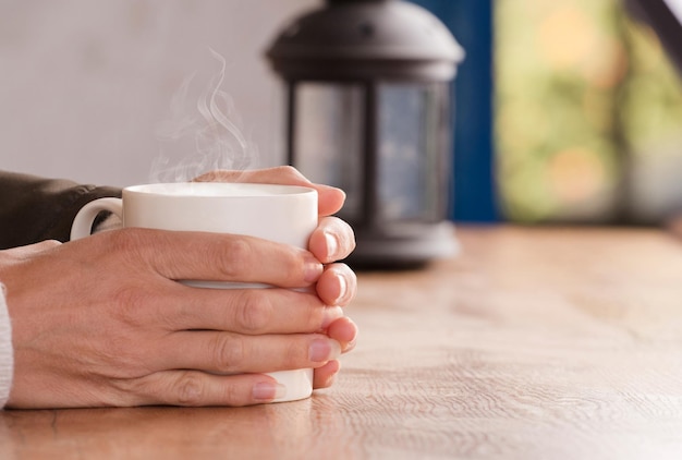 white cup with hot drink and smoke hands warming up from the heat at home Focus on the cup