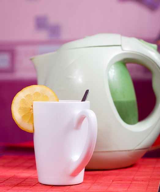 White cup with piece of lemon and kettle