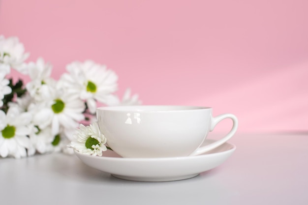 Foto una tazza bianca con un piatto si erge su uno sfondo rosa con fiori di crisantemo bianco