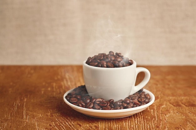 White cup with roasted coffee beans on wooden table. Copy Space