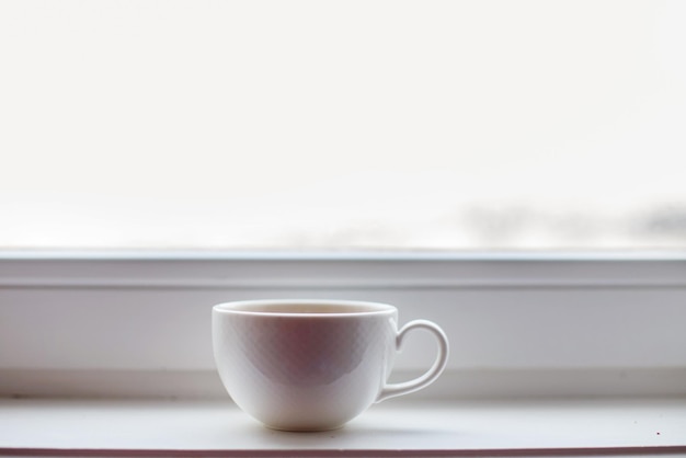 Белая чашка с чаем стоит на подоконнике на окне