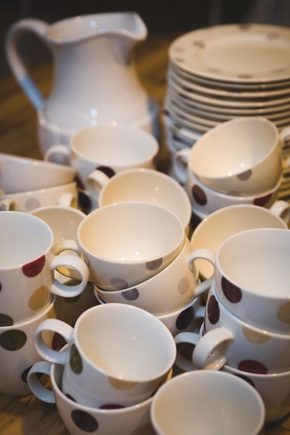 White cups with dark polka dots a stack of plates and a stylish jug on a wooden table