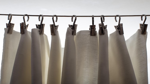 White curtain hangs on metal clothespins in natural light