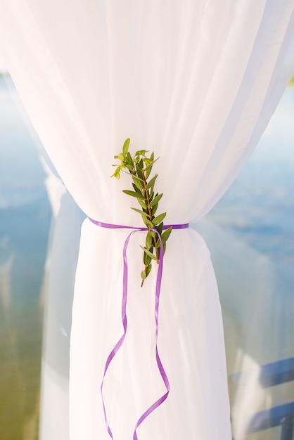 The white curtain is gathered under a purple satin ribbon with a sprig of green close-up. Interior detail