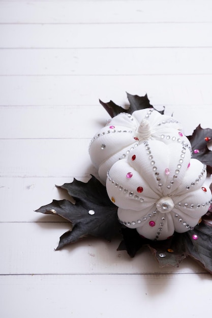 White decorative pumpkins with shiny stones and maple leaves on wooden background Thanksgiving day concept