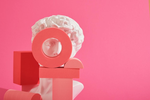 White decorative sculptural bust and several pink geometric coasters on a pink background geometric shapes forms. Exhibition podium, platform for product presentation