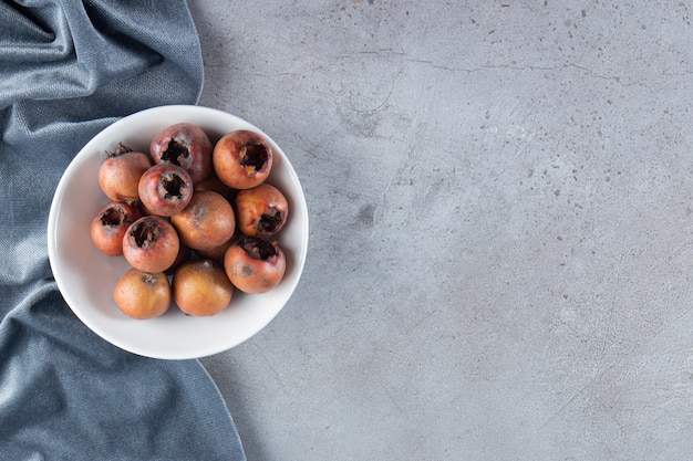 White deep plate of fresh medlar fruits on stone background. 