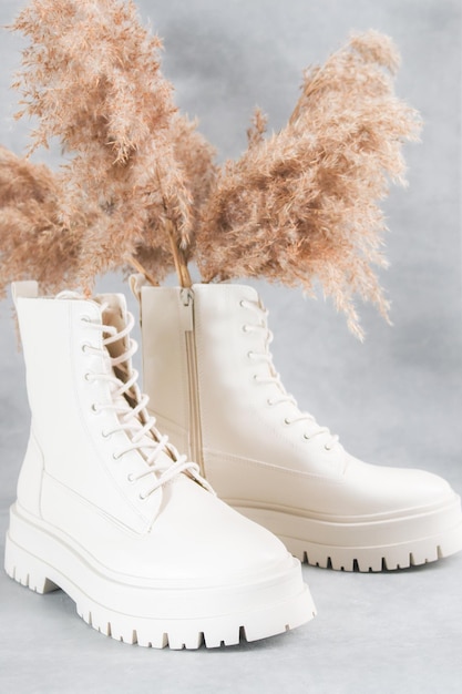 White demiseason boots and a dry cane branch on a gray cement background