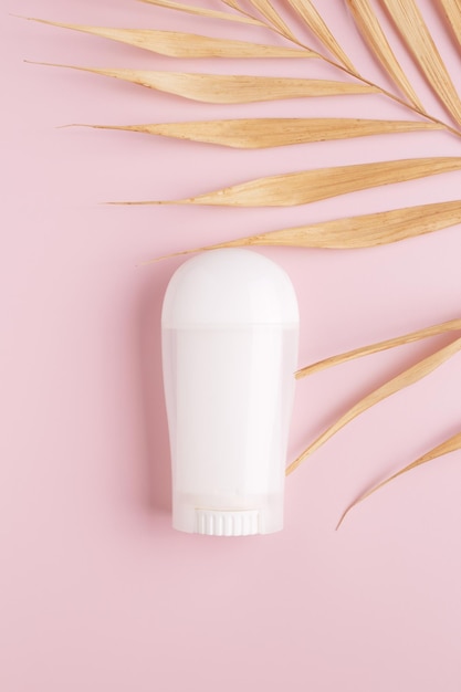 White deodorant and palm leaf on pink background