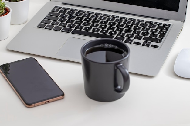 ラップトップスマートフォンとコーヒーのカップを備えた他の作業用品を備えた白いデスクオフィスデスクテーブル上のデザイナーワークスペースフラットレイの重要な要素