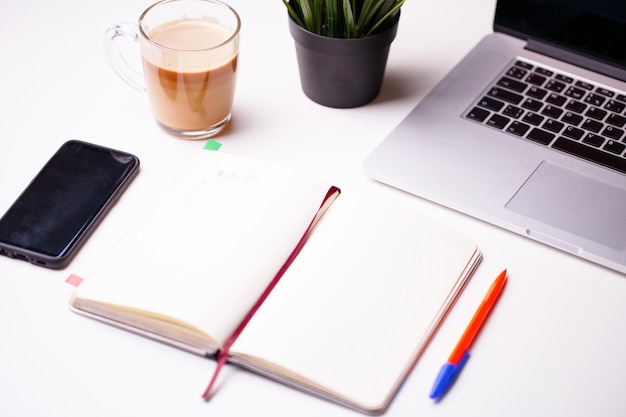 White desk with notebook blank notebook green flower phone and cup of coffee