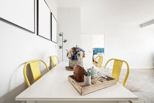 White dining table with crockery on a wooden tray and decorative dried flower centerpiece and metallic yellow chairs