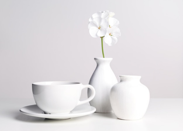 White dishes and a flower in a vase on a light background.