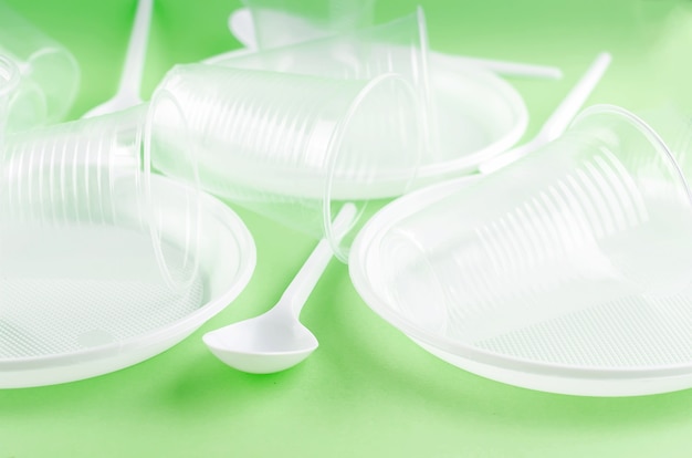 White Disposable cups, plates, forks, knives on light green background close-up - Environmental problem concept