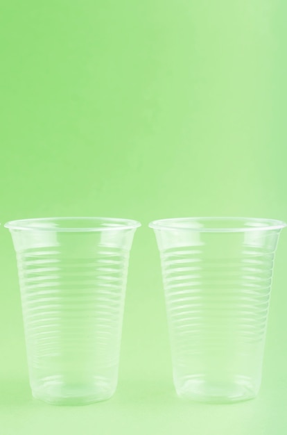 White Disposable cups, plates, forks, knives on light green background close-up -