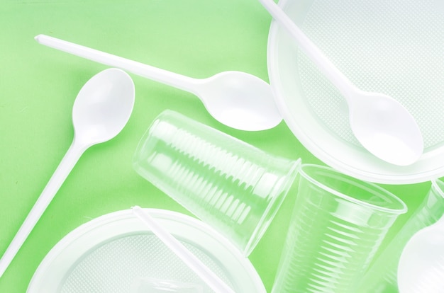 White Disposable cups, plates, forks, knives on light green background closeup