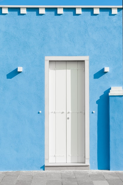 White door on the blue painted facade of the house. colorful architecture in burano island, venice, italy