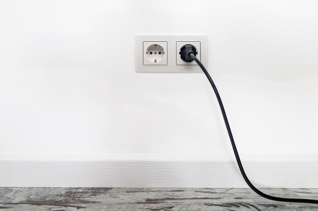 Photo white double outlet installed on white wall with inserted black electrical plug front view