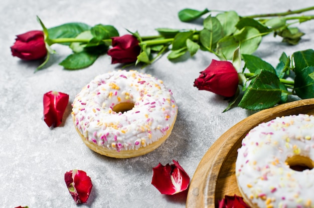 White doughnuts with sprinkles, decorated with a red rose.