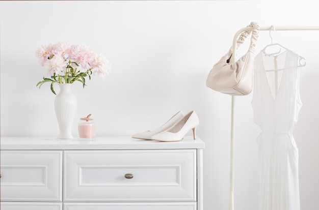 White dresser with clothes and flowers in white room
