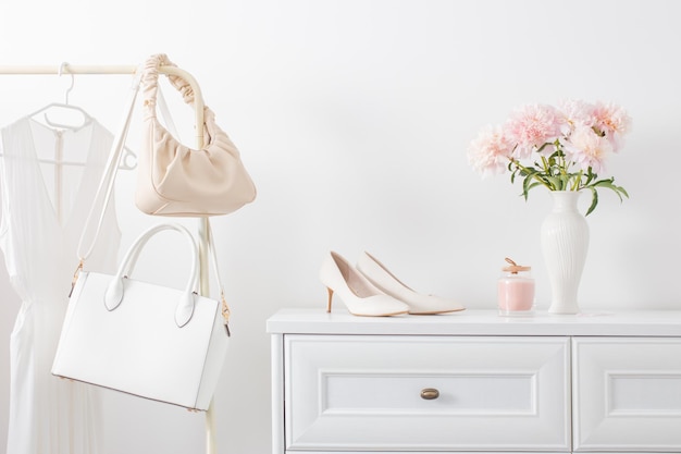 White dresser with clothes and flowers in white room