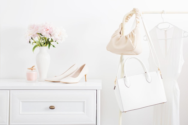 White dresser with clothes and flowers in white room