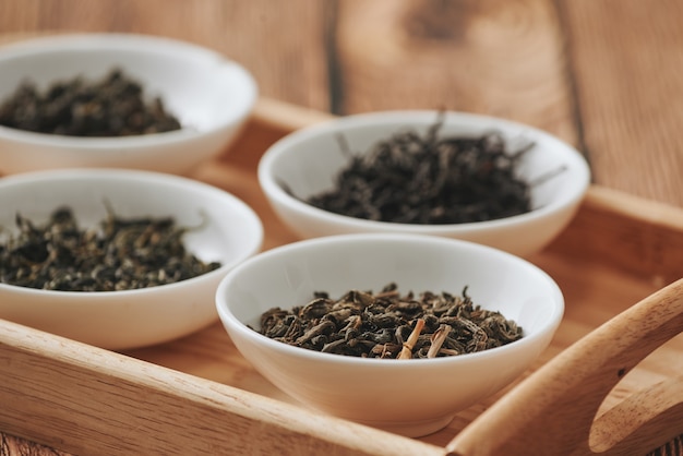 The white drinking bowls of assortment of dry tea in order on wooden background