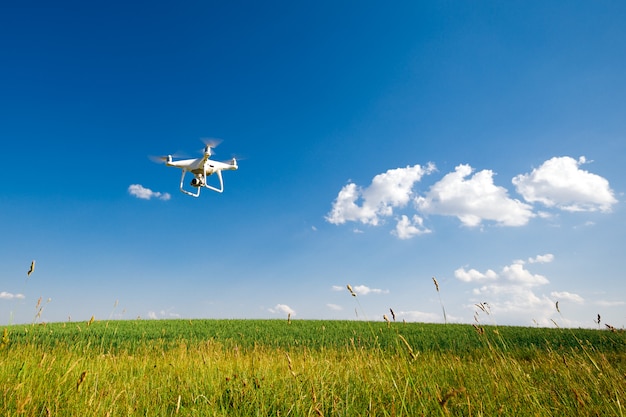 The white drone in hands at the man isolated against the background of the green field